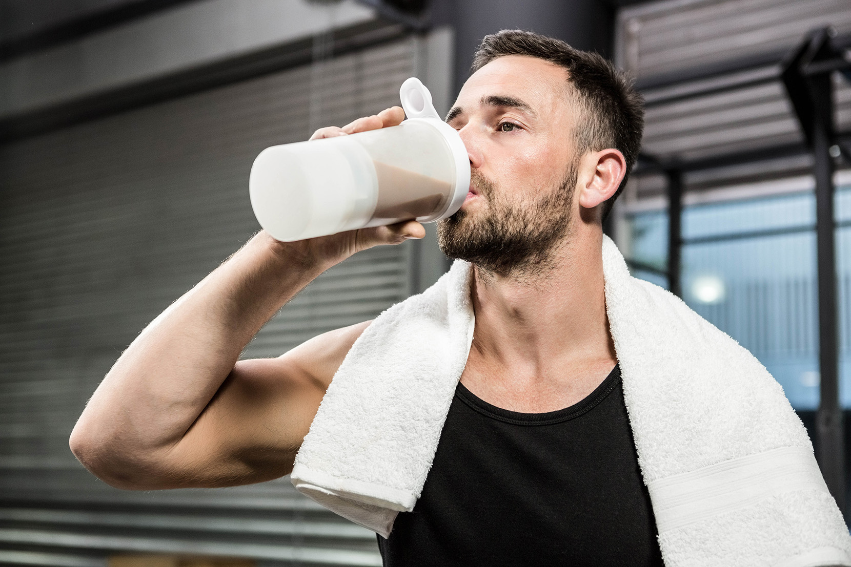 fit muž pije proteínový nápoj vo fitku